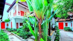 A traditional house with a red door and balcony, surrounded by lush greenery and a stone pathway. - Villa Wat Damnak (Siem Reap)