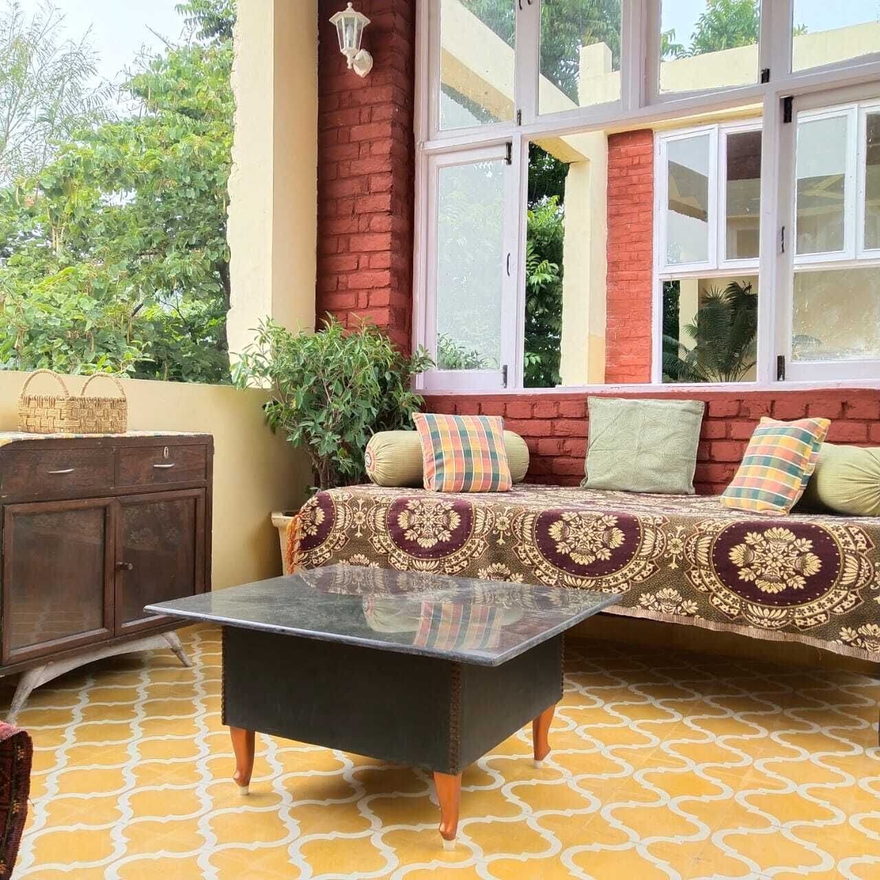A cozy outdoor seating area with a sofa, cushions, and a glass-top table.