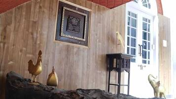 Un interior rústico con una pared de madera, un cuadro enmarcado, un gallo dorado, un cerdo dorado y una mesa negra.