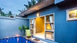 A poolside area with a blue pool, a wooden deck, and a building with large windows and a door. - Kawans Inn Lembongan by Zuzu (Lembongan Island)