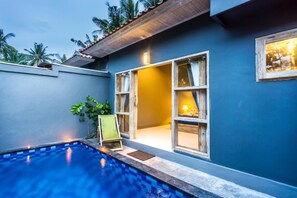 A poolside area with a blue pool, a wooden deck, and a building with large windows and a door. - Kawans Inn Lembongan by Zuzu (Lembongan Island)