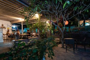 An outdoor seating area with tables and chairs, surrounded by greenery and a wooden pergola structure. - Kawans Inn Lembongan by Zuzu (Lembongan Island)