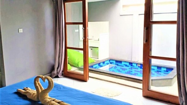 A room with a bed, a heart-shaped towel sculpture, and a view of a swimming pool through glass doors. - Kawans Inn Lembongan by Zuzu (Lembongan Island)