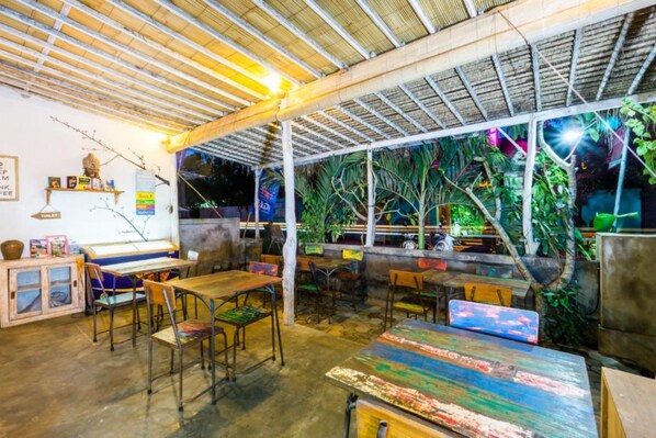 An indoor dining area with tables and chairs, a counter with a display, and a view of the outdoors through a covered patio. - Kawans Inn Lembongan by Zuzu (Lembongan Island)