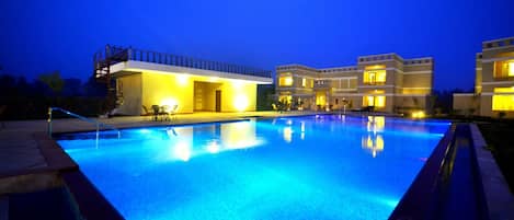 A swimming pool with a clear blue water surface, surrounded by a building with multiple balconies and outdoor seating areas.