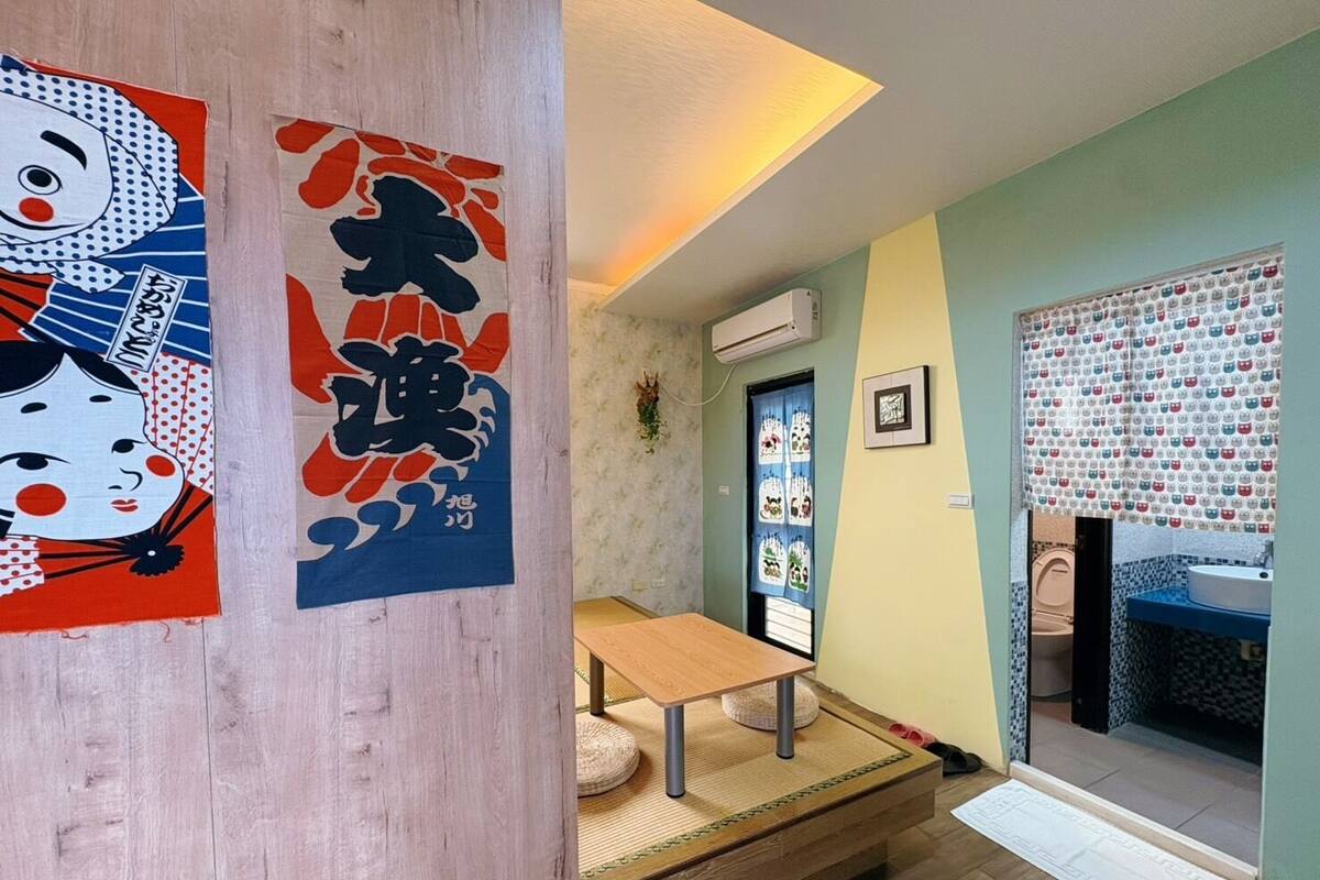 Una habitación con piso de madera, un futón de tatami, una mesita pequeña y una puerta corrediza tradicional japonesa.