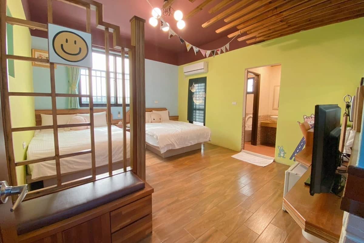 Una habitación con dos camas, piso de madera, televisor y baño visible a través de una puerta abierta.