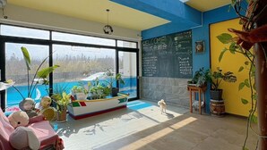 A spacious living area with a large window, a cozy seating area with a pink sofa, and a variety of potted plants. - Big Fish House (Magong)