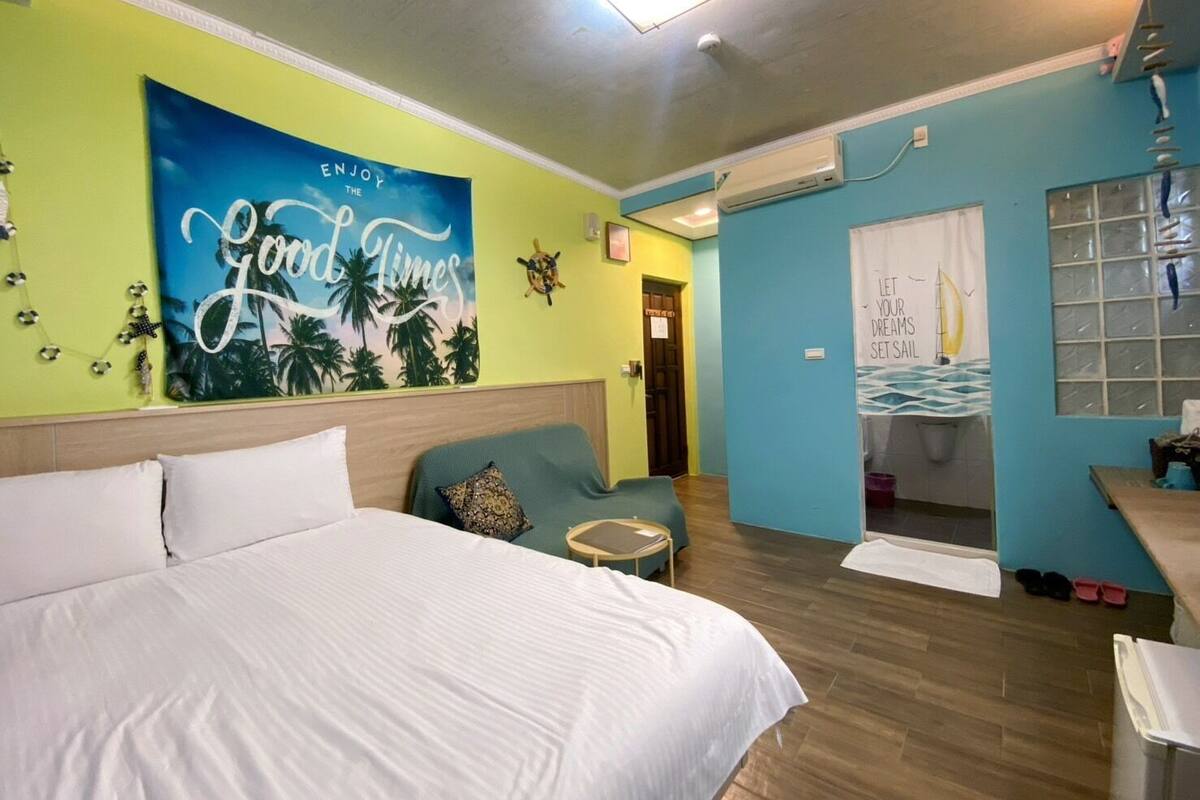 Habitación de hotel con una cama grande, un sofá, una mesita y una pared con un cartel que dice 'Good Times'.