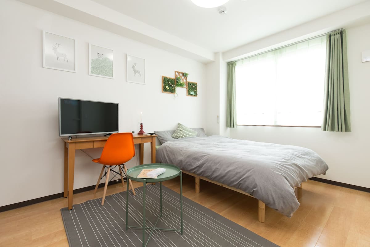 Un dormitorio moderno con una cama, un escritorio con computadora, una silla y un televisor.