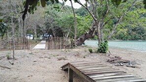 A wooden dock extending into a body of water, surrounded by trees and a gravel path leading to a row of buildings. - Tropical Eco Camping (Langkawi)