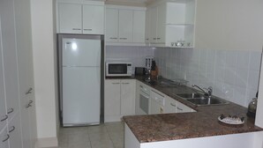 Una cocina con armarios blancos, un refrigerador de acero inoxidable, un microondas y una encimera de granito.