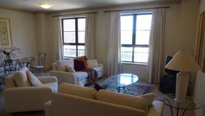 Una sala de estar con un sofá, sillones, una mesa de centro de vidrio y un televisor.