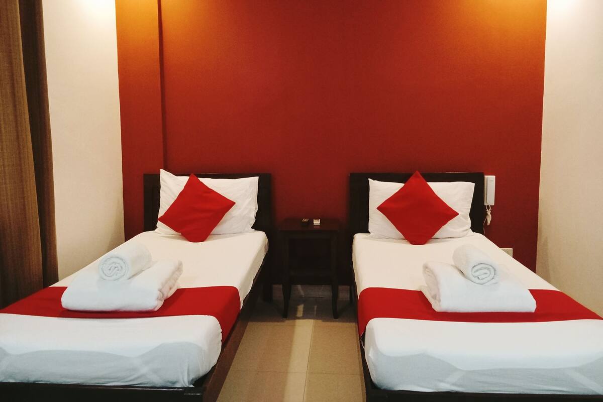 Ett hotellrum med två separata sängar, båda med vita sängkläder och röda kuddar.