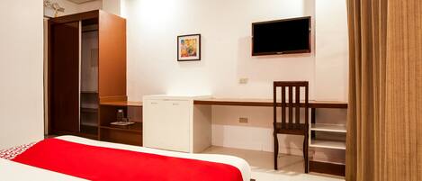 A hotel room with a bed, a desk, a chair, a TV, and a wardrobe.