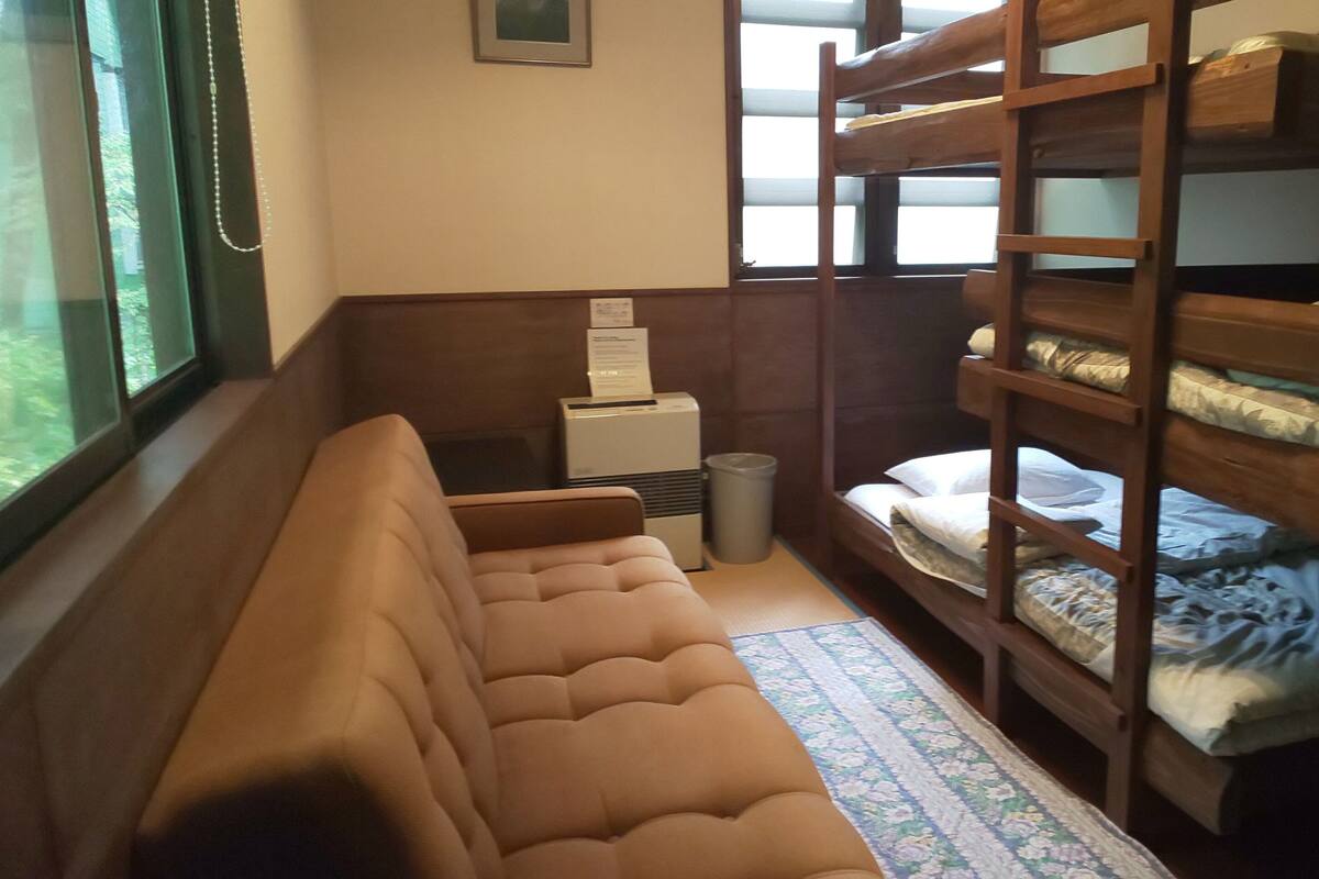 A bunk bed room with a sofa, a small table, and a trash bin.