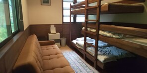 A bunk bed room with a sofa, a small table, and a trash bin.