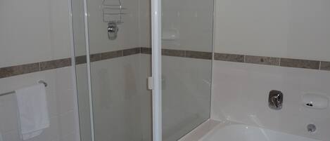 Une salle de bain avec une douche à parois de verre, une baignoire blanche et un porte-serviettes.