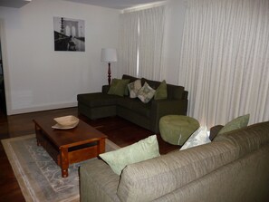 A living room with a sofa, a coffee table, and a lamp. - City Escape 3BD in Adelaides East End 6 (Adelaide)