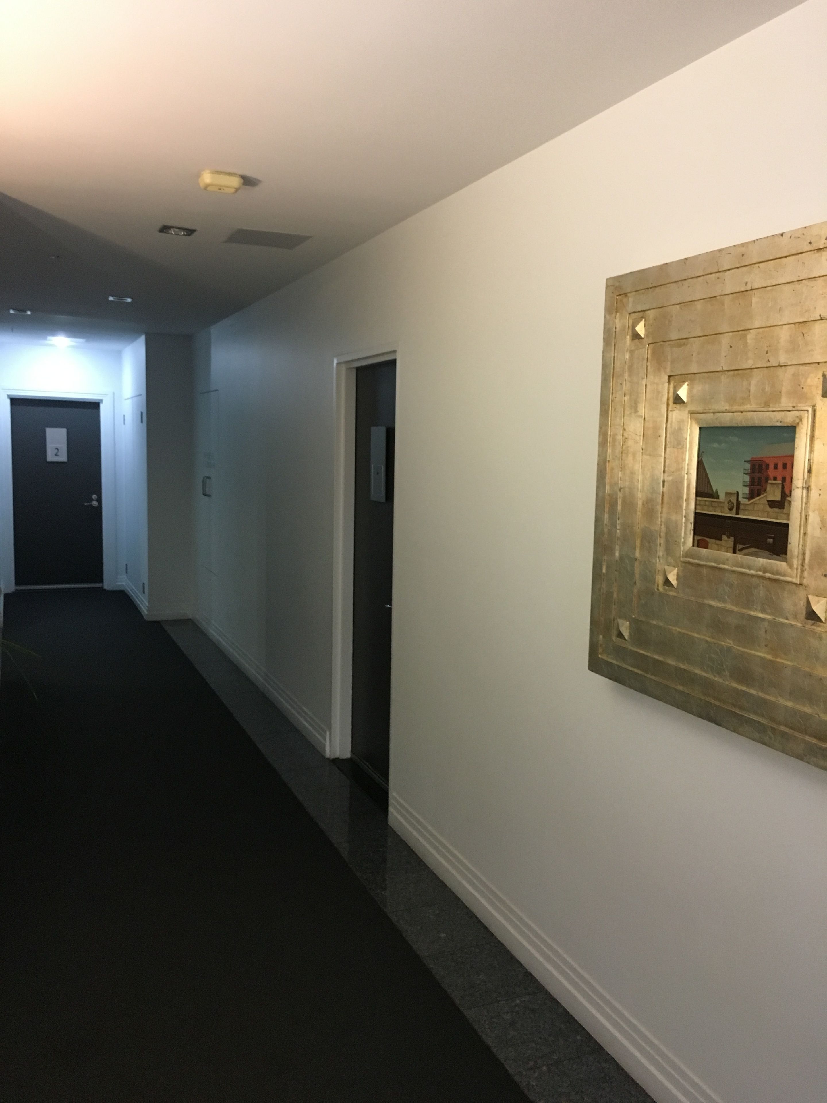 Ein Korridor mit einer Tür, auf der die Aufschrift „2“ steht, und einem gerahmten Bild an der Wand.