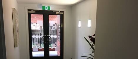 Un pasillo con alfombra negra que conduce a una puerta con un panel de vidrio. Arriba de la puerta, un letrero de salida verde.