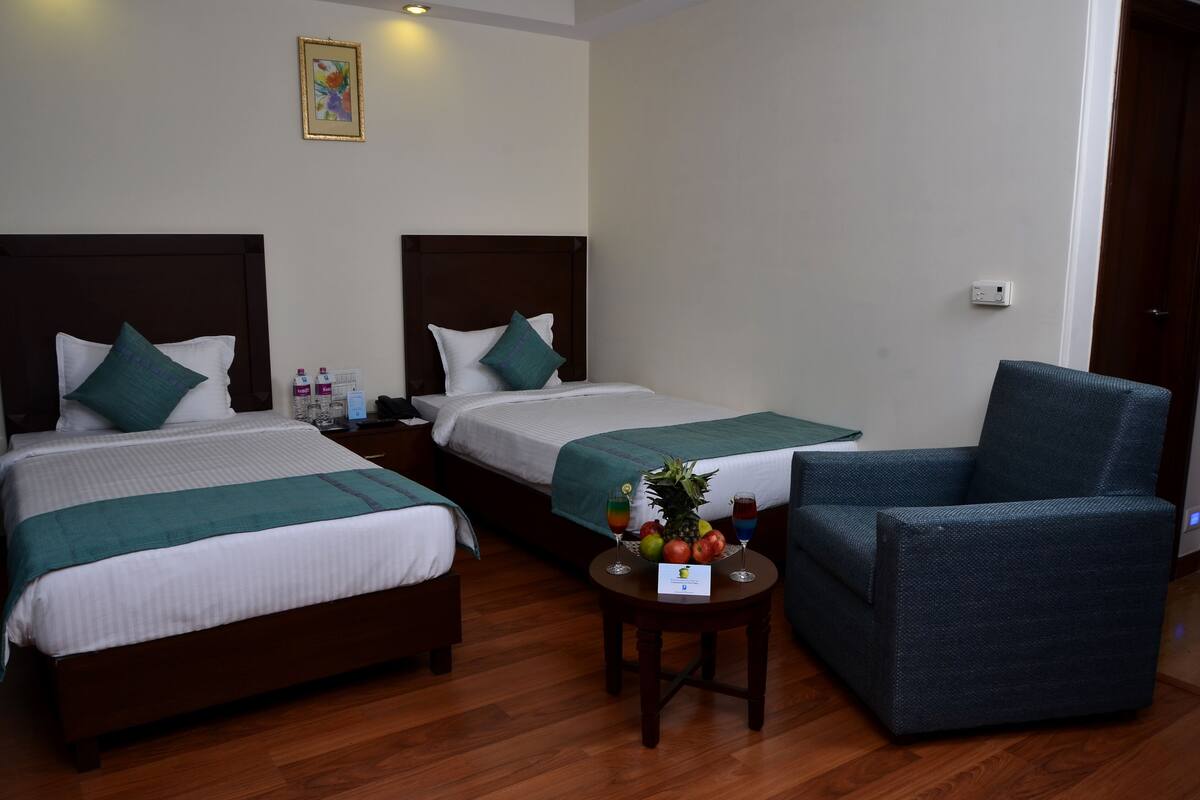 Una habitación de hotel con dos camas, una silla y una mesita con fruta y bebidas.