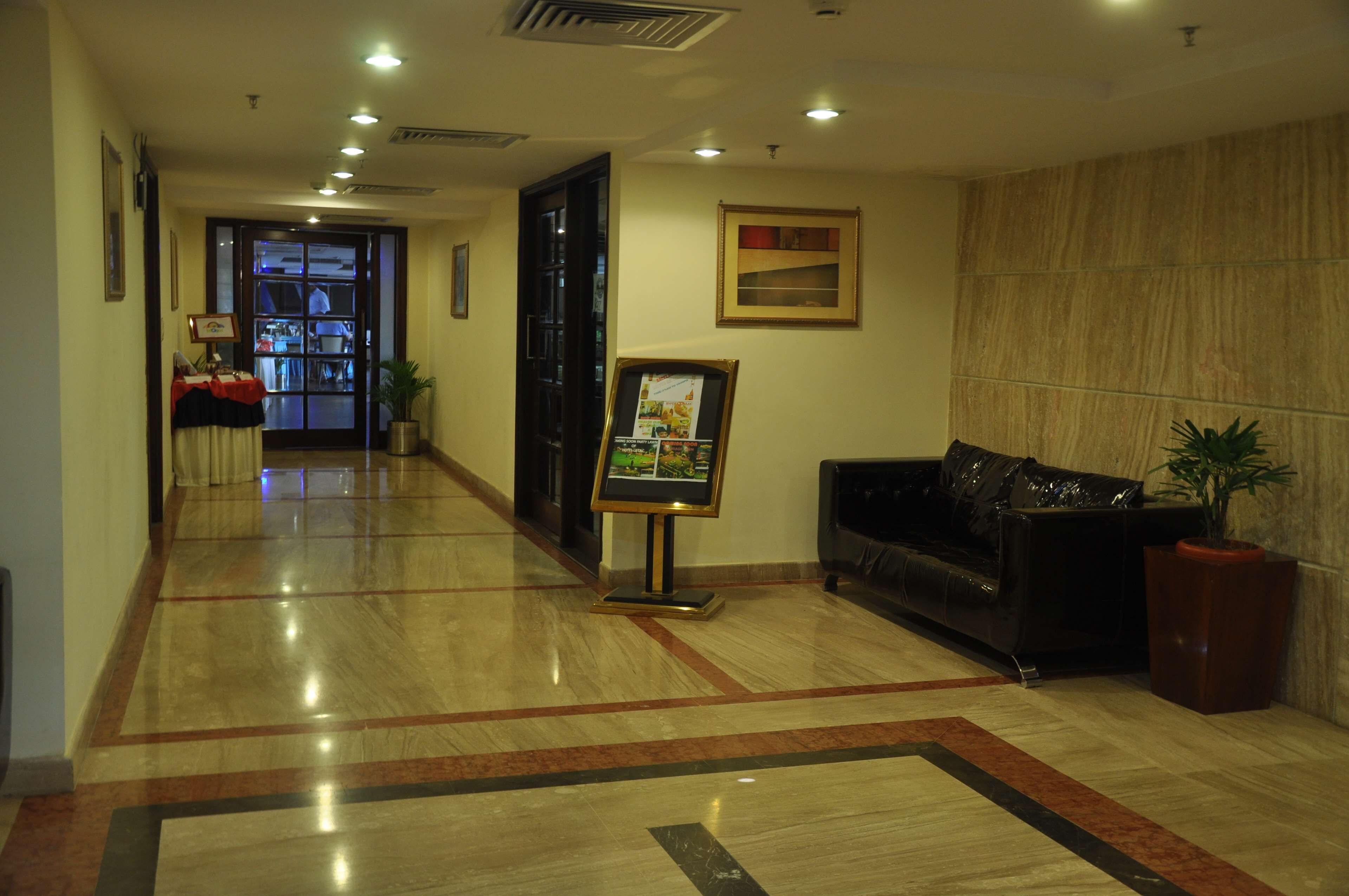 A hotel lobby with a reception desk, a black leather sofa, a potted plant, and a framed picture on the wall.