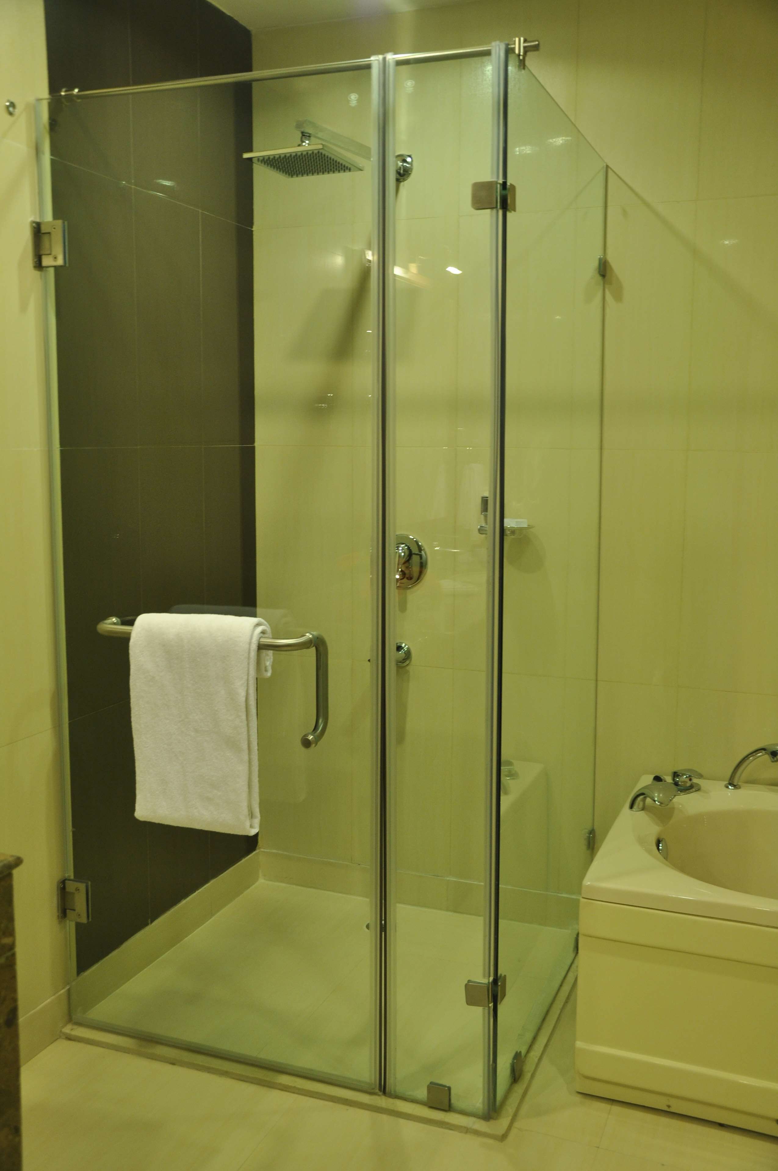 A glass-enclosed shower with a white towel on the door handle, a glass door, and a bathtub with a faucet.