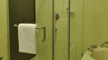 A glass-enclosed shower with a white towel on the door handle, a glass door, and a bathtub with a faucet.