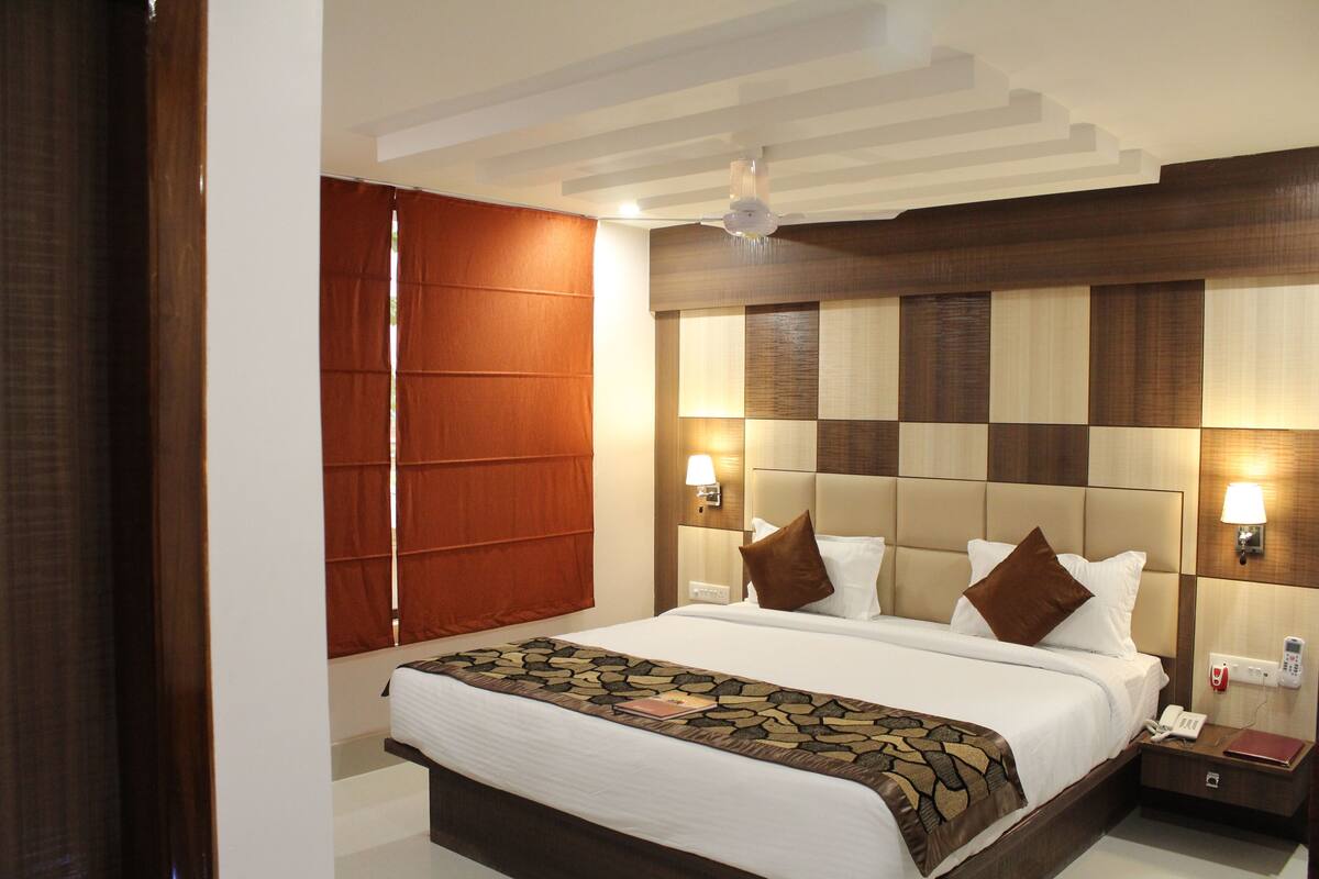 A hotel room with a large bed, a nightstand, a telephone, and a wall-mounted lamp.