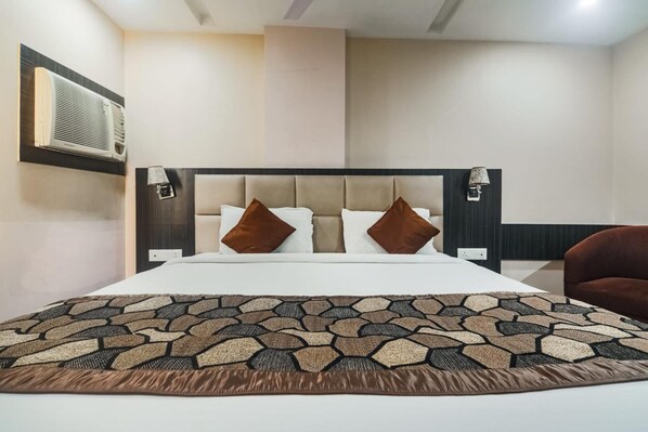 Habitación de hotel con una cama grande, cabecera con lámparas de pared, colcha estampada y una silla marrón.