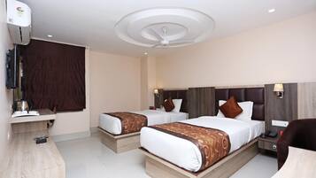 A hotel room with two beds, a desk, a chair, a ceiling fan, and a window with curtains.
