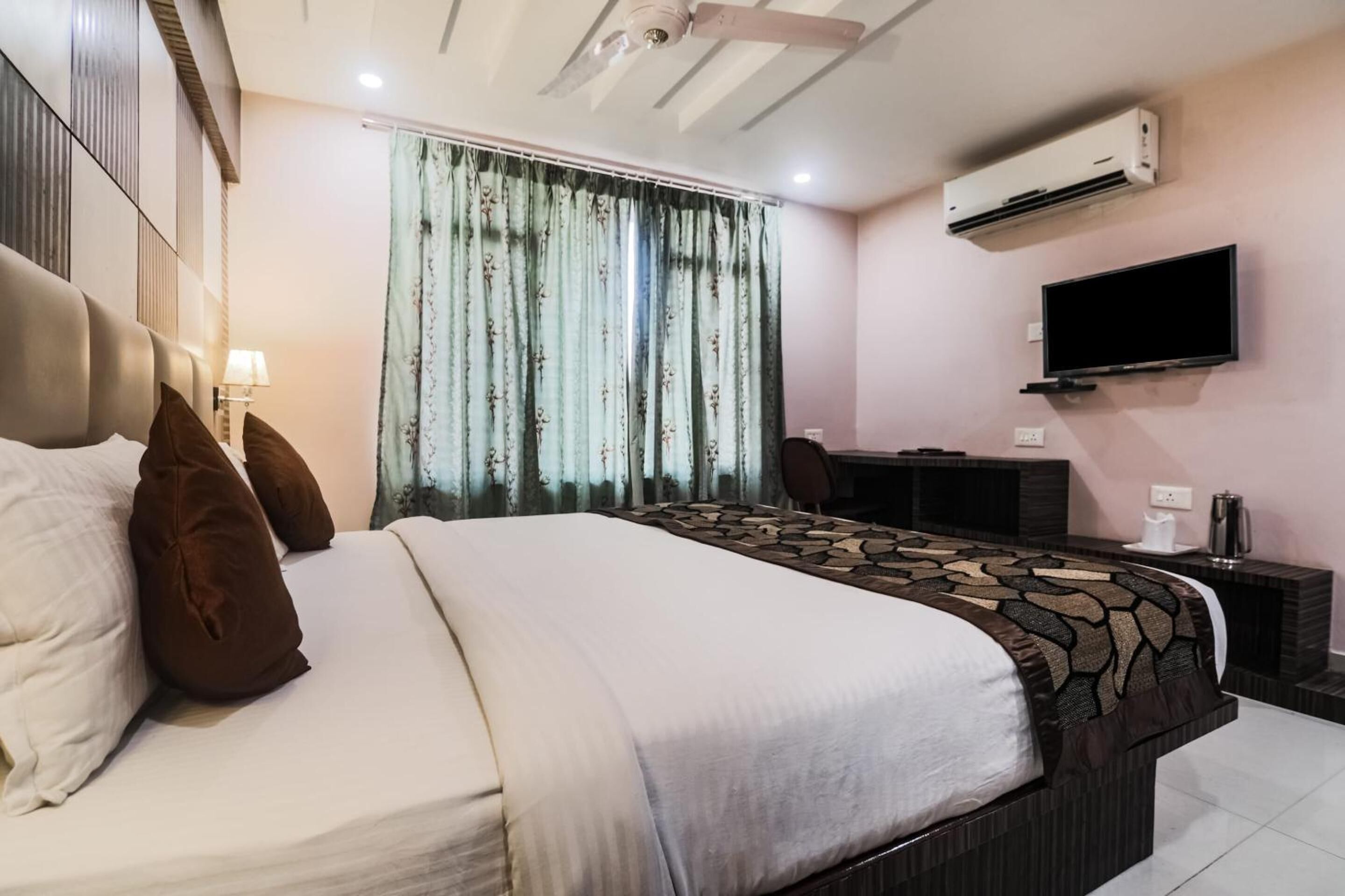 Una habitación de hotel con cama, escritorio, televisión y aire acondicionado.