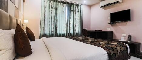 Una habitación de hotel con cama, escritorio, televisión y aire acondicionado.
