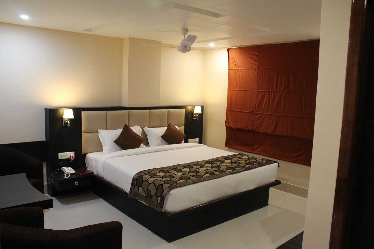 A hotel room with a large bed, a bedside table with a lamp, a phone, and a chair.