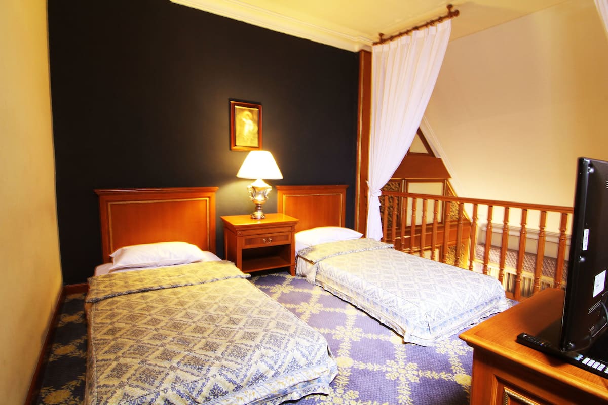 A hotel room with two beds, a nightstand with a lamp, a television, and a wooden staircase.