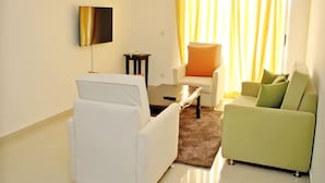 A modern living room with a white sofa, a green sofa, a coffee table, and a TV mounted on the wall. - Résidence Mohili (Abidjan)