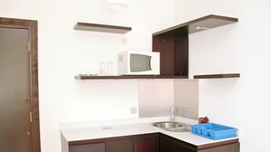 A compact kitchen with dark wood cabinets, a white countertop, a stainless steel sink, and a microwave on an upper shelf. - Résidence Mohili (Abidjan)