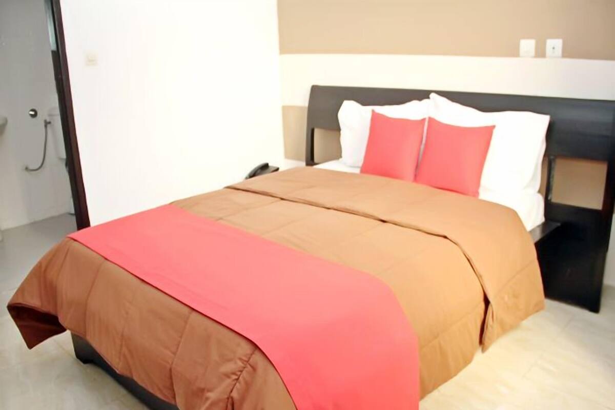 A neatly made bed with a brown and red bedspread, a black headboard, and white pillows.