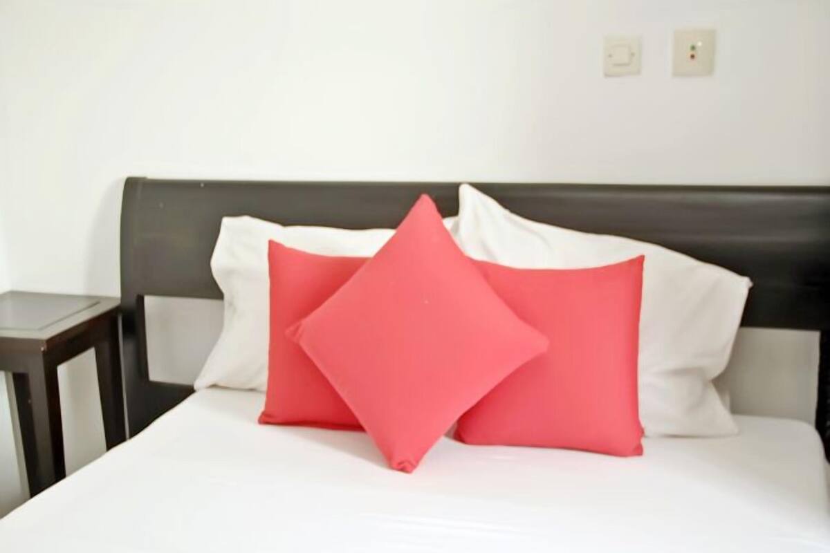 A bed with white bedding and two red pillows.