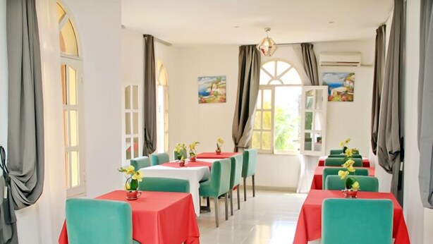 A dining area with tables covered in red and green tablecloths, chairs in matching colors, and yellow flowers on each table. - Résidence Mohili (Abidjan)
