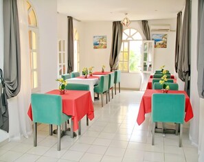 A dining area with tables covered in red and green tablecloths, chairs in matching colors, and yellow flowers on each table. - Résidence Mohili (Abidjan)