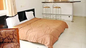 A hotel room with a bed, a chair, a small table, and a window with curtains. - Résidence Mohili (Abidjan)
