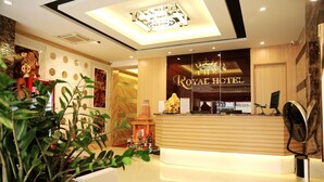 A reception area with a wooden reception desk, a large window with the Royal Hotel name, and a decorative statue. - The Royal Hotel (Hanoi)
