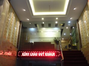 A hotel entrance with a modern design, featuring a glass facade, a staircase, and a digital sign displaying the hotel's name. - The Royal Hotel (Hanoi)