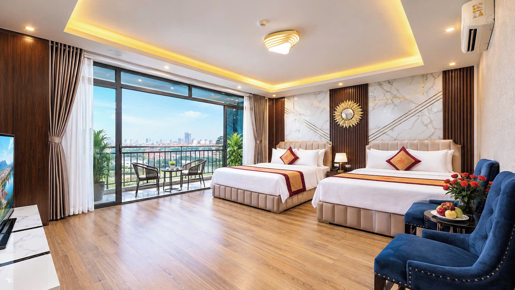 A hotel room with two beds, a TV, a balcony with a city view, and a dining area.