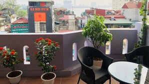 A terrace with potted plants, a table, and chairs. - The Royal Hotel (Hanoi)