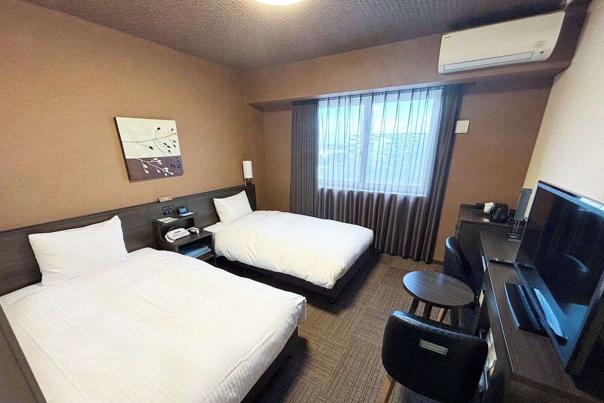Ein Hotelzimmer mit zwei Betten, einem Schreibtisch mit Fernseher und einer Klimaanlage.