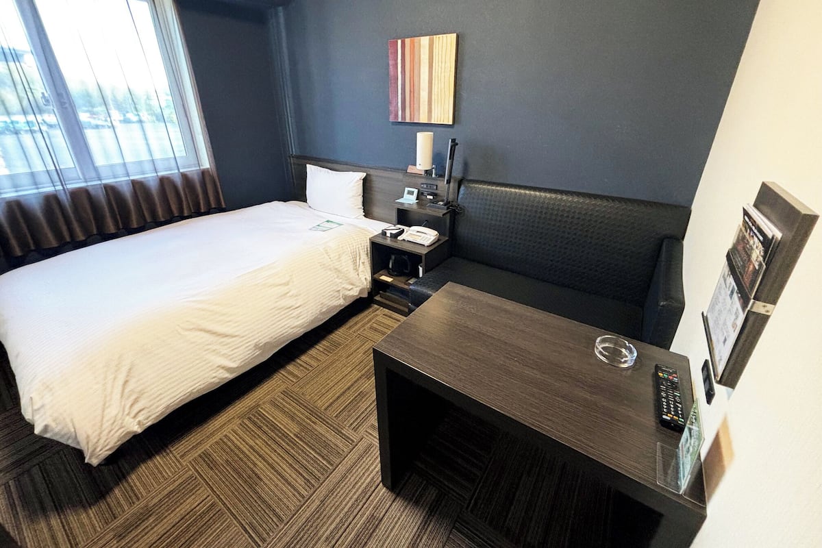 Ein Hotelzimmer mit Bett, Nachttisch, Lampe und Blick ins Freie.