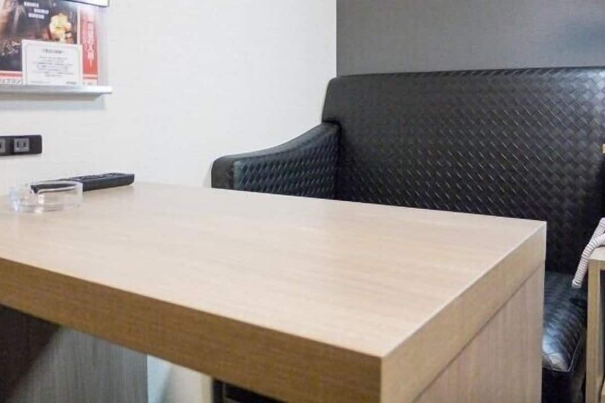 Ein Hotelrezeptionstresen mit Holzbeschichtung, ein schwarzer Bürostuhl, ein gerahmtes Zertifikat an der Wand und ein Telefon auf einem kleinen Tisch.